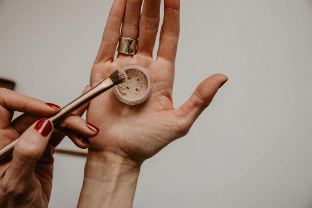 hands tapping excess makeup powder off a makeup brush