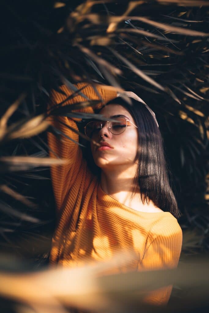 woman in yellow shirt and orange makeup posing between spiky leaves